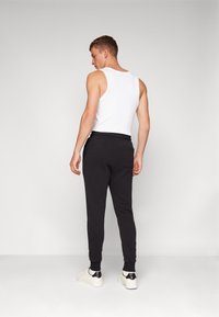 Schwarze Sporthosen mit elastischem Bund und Bündchen, kombiniert mit einem weißen Tanktop. Die Schuhe haben einen schwarzen Akzent an der Ferse.