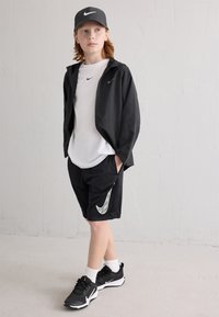 Čierna Nike zipsová bunda, biele tričko, čierne kraťasy s bielym logom Nike a čierne tenisky s bielymi akcentmi, umiestnené na neutrálnom pozadí.