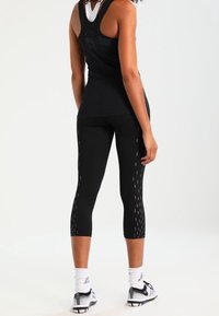 Zwarte atletische tanktop en cropped leggings met gestructureerde patronen en reflecterende accenten. Model gezien van achteren met sportschoenen.