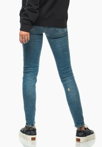 Smaljeans i blekt blå denim med en lätt sliten detalj, kombinerat med svarta sneakers med ett mönstrat design och vit sula.