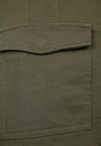 Olive green fabric with a ribbed texture and a patch pocket stitched at the top. Features straight edges and subtle seam detailing.