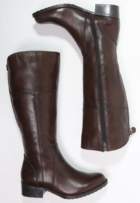 Bottes montantes en cuir marron avec une tige droite, une fermeture éclair latérale et un petit talon bloc. Texture lisse avec un détail de coutures discrètes.