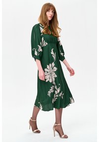 Zielona sukienka midi w kwiaty z bufkami na rękawach i dopasowanym stanem, ozdobiona dużymi białymi kwiatowymi nadrukami oraz wykonana z lekkiego, lejącego się materiału.