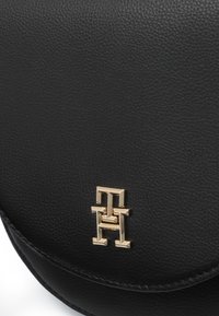 Black leather handbag featuring a gold logo embossed on the front, with a smooth texture and rounded flap design.