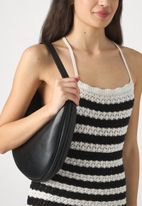 Große schwarze Lederhandtasche mit einer geschwungenen Form und einer glatten Textur, gehalten von einer Person, die ein schwarz-weiß gestreiftes Oberteil trägt.