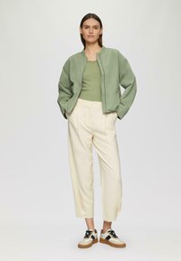 Hellgrüne Bomberjacke, tailliertes grünes Oberteil, cremefarbene Hose und Sneaker mit schwarzen und beigen Akzenten. Lässige Passform, glatte Texturen.