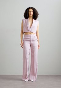 Top court sans manches rose clair et pantalon large taille haute. Tissu lisse, design minimaliste et coupe ajustée. Chaussures blanches.