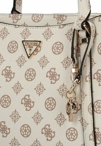 Sac à main blanc texturé avec un motif logo beige, présentant un logo triangle doré et un charme en forme de clé. Matériau lisse, forme structurée et accents contrastants.