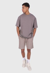 Szary, oversize'owy t-shirt z okrągłym dekoltem, zestawiony z beżowymi, prążkowanymi szortami. Model nosi białe sneakersy oraz białe skarpetki do kolan.