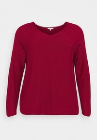 Pull rouge à manches longues avec un col en V, conçu à partir d'un tissu en tricot texturé. Présente un petit logo sur la poitrine.