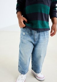 Heledad sinised teksad kulunud detailidega; lahtine lõige ja lai säärega stiil, mis on kombineeritud valgete tossude ja mereväe triibulise kampsuniga.