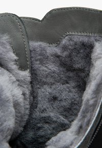 Botte en cuir gris avec une doublure intérieure douce et moelleuse de couleur grise. Présente un bord supérieur festonné et des détails cousus le long des coutures.