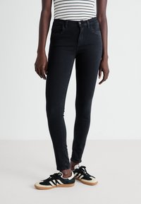 Jeans skinny negros de talle alto, con cinco bolsillos y detalles de costura sutil, combinados con zapatillas retro blanco y negro.