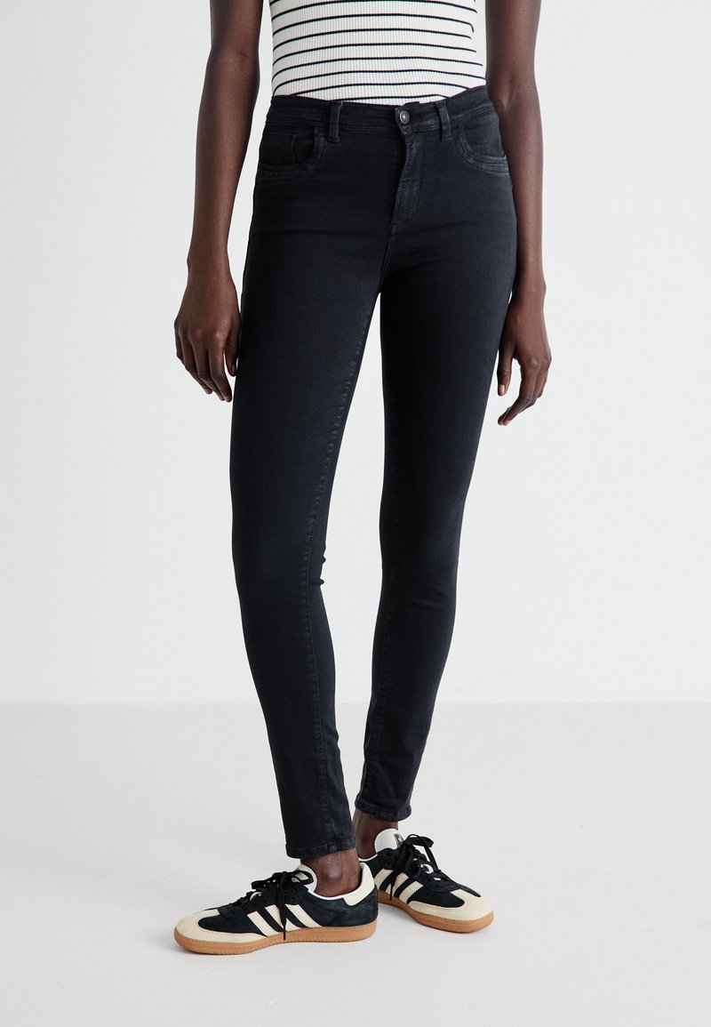 Jeans skinny negros de talle alto, con cinco bolsillos y detalles de costura sutil, combinados con zapatillas retro blanco y negro.
