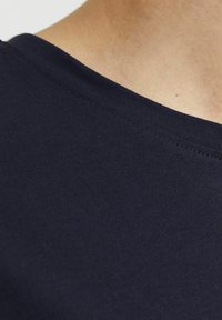 Tmavě námořnická bavlněná tričkovina, detailní záběr hladké textury a žebrovaného výstřihu, s viditelnými detaily šití.