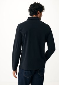 Zwarte langemouwen shirt met een kraaghalslijn, een gladde textuur en zijsplitten, gecombineerd met donkerblauwe spijkerbroek.