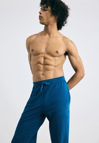 Lichte blauwe broek met een elastische tailleband en koord. Gemaakt van een gladde stof, met een logo aan de linkerkant.