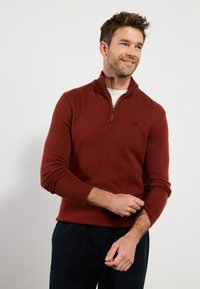 Rostfarbener Zip-Kragen-Pullover aus weichem Stoff mit gerippten Bündchen, der ein kleines Logo-Detail auf der Brust und eine normale Passform aufweist.