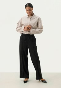 Chemise à rayures beige et marron, associée à un pantalon noir à taille élastique. Présente une coupe décontractée et des manches longues. Élégantes chaussures à talons noires.