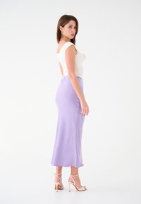 Top bianco arricciato con maniche corte; gonna midi fluida di color lavanda; modella che indossa scarpe con tacco nude e strappy; texture liscia.