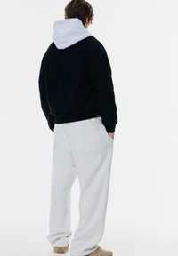 Čierna mikina s šedou kapucňou, skombinovaná s svetlo šedými, voľne strihanými teplákmi s zadnou kapsou. Béžové topánky dopĺňajú outfit.