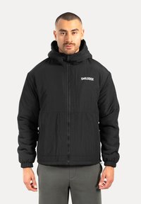 Czarna puchowa kurtka z zamkiem z przodu, elastycznymi mankietami i kapturem. Posiada teksturowany materiał oraz białe logo na klatce piersiowej.