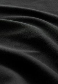 Tissu noir à la texture douce et lisse montré en gros plan, mettant en valeur des plis délicats et des reflets lumineux subtils.
