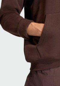 Hnedá mikina s mäkkou textúrou, vo voľnom strihu a s rebrovanými manžetami. Má prednú kapsu a mierne predĺžený zadný lem.