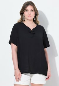 Top corto nero a maniche corte con scollo a V e dettaglio a fiocco all'ascella, realizzato in un tessuto morbido e leggero. Design semplice e dal taglio rilassato.