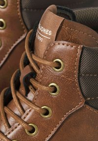 Brune læder høje sneakers med guld øjer, brune snørebånd, en tekstureret finish og kontrasterende mesh-detaljer på siderne.