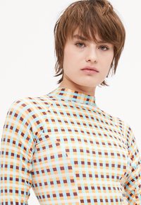 Colorful fitted top with a high neckline, featuring a grid pattern in light blue, orange, and brown. Smooth texture and stretchy material.