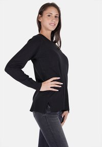 Maglione nero a maniche lunghe con scollo rotondo, orlo a coste e spacchi laterali, realizzato in un tessuto morbido e flessibile. Abbinato a jeans scuri.