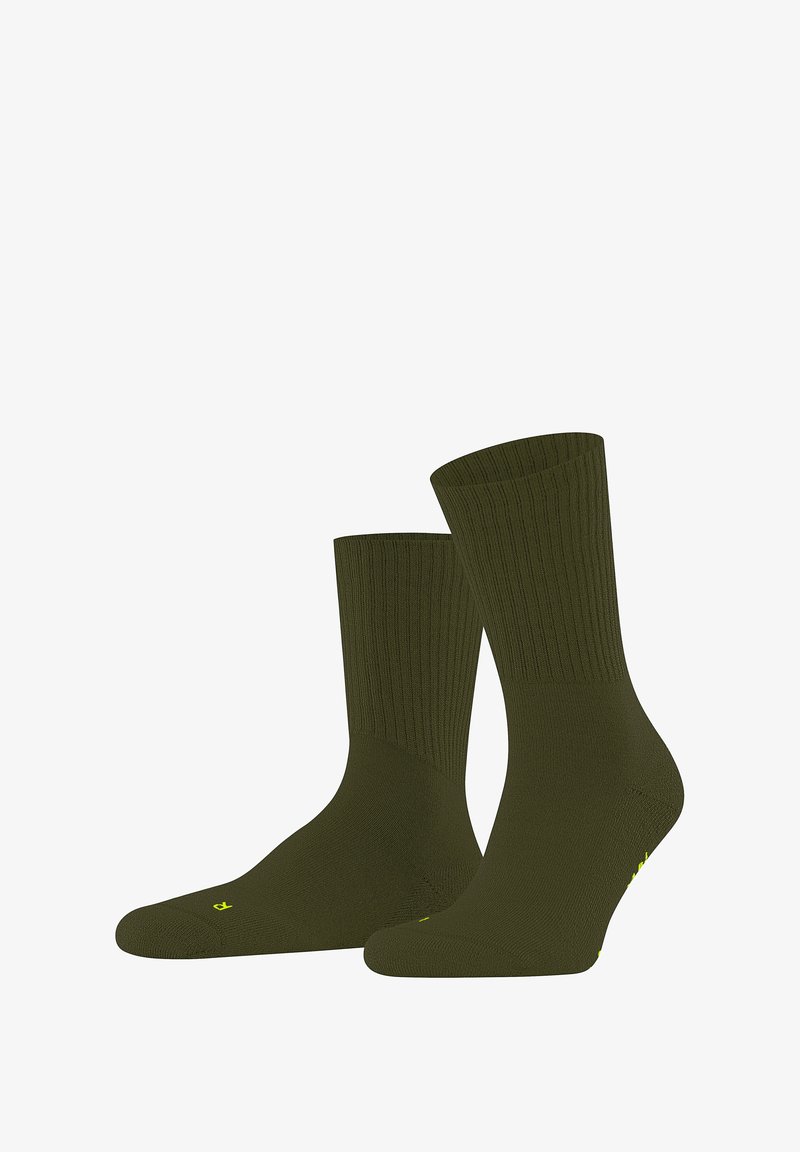 Chaussettes côtelées vert olive exposées debout, mettant en valeur leur texture lisse et leur léger éclat, avec un petit logo jaune sur le côté.