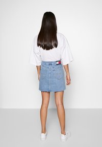 Jeansrock mit rohem Saum, hellblauem Farbton und klassischem Fünf-Taschen-Design. Kombiniert mit einem lockeren weißen T-Shirt und weißen Turnschuhen.