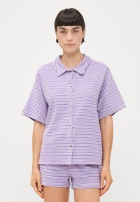 Camicetta a maniche corte a righe viola e bianche con colletto, abbinata a pantaloni della stessa fantasia. Tessuto morbido e vestibilità comoda.