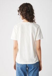 Camiseta de algodón color crema con mangas cortas y cuello redondo, que presenta una textura suave y un corte relajado, combinada con unos vaqueros de mezclilla azules.