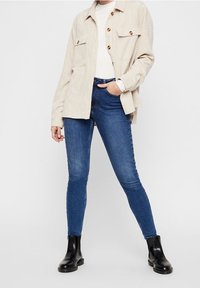 Beige kordjacka i manchester med två framfickor, kombinerad med mörkblå slim jeans och svarta ankelstövlar. Enkel, modern design.