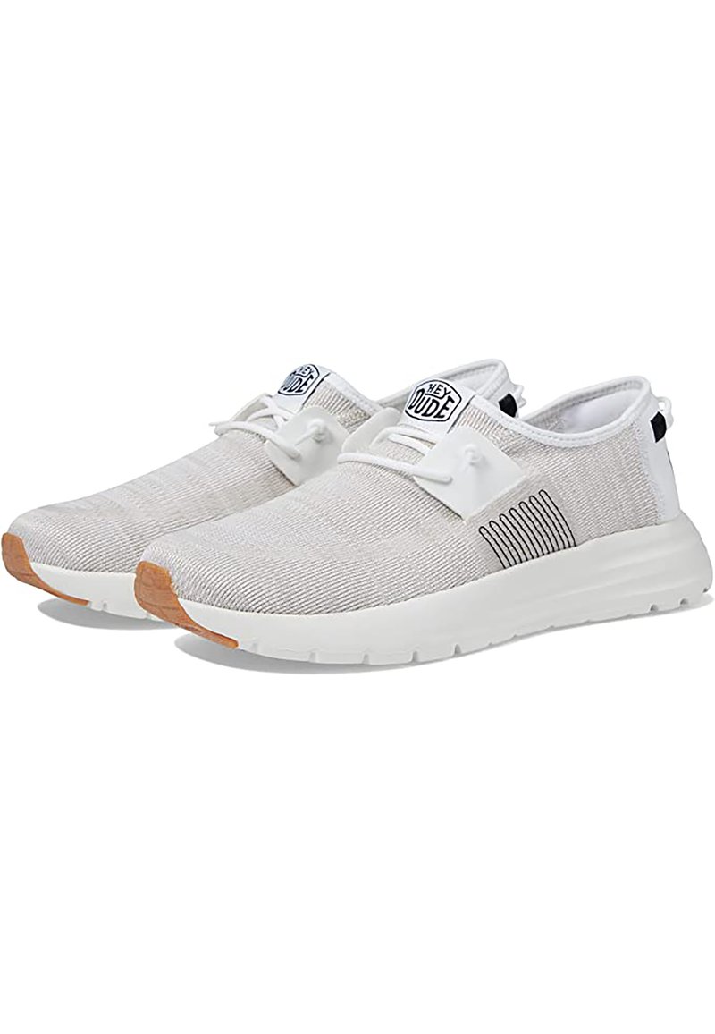 Scarpe da ginnastica leggere beige con parte superiore in maglia testurizzata, suola bianca e dettagli neri a strisce. Presentano un logo e un sistema di allacciatura minimale.