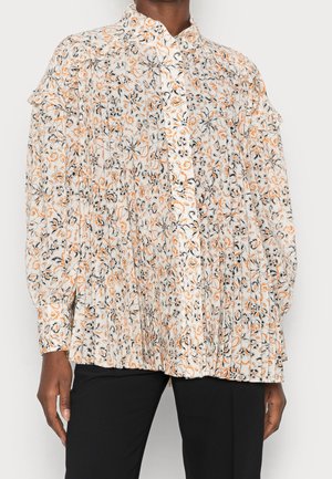 Blouse florale avec une base blanche, des motifs orange et noirs, des manches longues, un bouton sur le devant, et des détails de volants aux épaules.