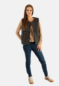 Gilet in pelliccia sintetica grigia sopra una maglietta a maniche lunghe beige, abbinato a jeans scuri e sneaker beige con dettagli bordeaux. Design semplice e texturizzato.