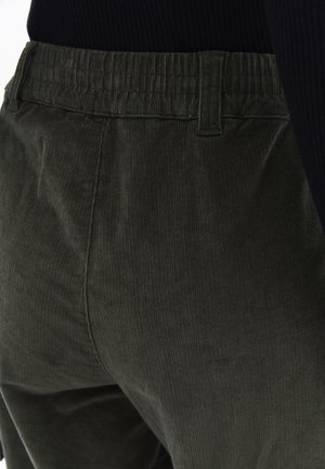 Donkergroene corduroy broek met een ribbelstructuur, voorzien van een elektrische tailleband en zijzakken. Middenhoogte pasvorm, met focus op de details aan de achterkant.