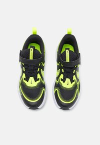 Baskets de sport noires et vert néon avec une tige en mesh, un col rembourré et une semelle texturée, dotées d'une sangle et d'accents blancs contrastants.