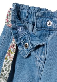 Cintura de denim azul claro con fruncido elástico, que presenta un acento de tela floral en el interior y un cierre de botón a presión metálico.