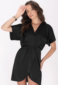 Rochie neagră, tip wrap, confecționată dintr-un material neted, cu mâneci scurte, decolteu adânc în V și o fante pe partea laterală a tivului pentru un plus de detaliu.