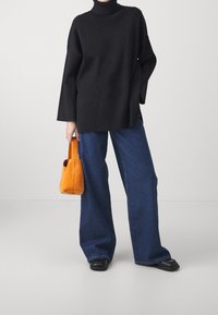 Svart ribbad polotröja, oversized passform, matchad med vida blå denimjeans och en orange mockaväska. Svarta platta skor.