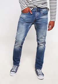 Jeans de mezclilla azul con un lavado deslavado, diseño de cinco bolsillos y corte recto, combinados con zapatillas altas oscuras.