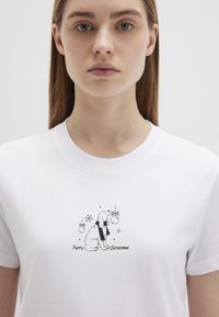 Weißes Baumwoll-T-Shirt mit einem schwarzen grafischen Design eines Hundes, der einen Schal trägt, umgeben von Feiertagsornamenten und dem Text "Frohe Weihnachten für Fellfreunde."