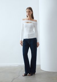 Balta ribota topiņa bez plecu ar izgriezumu un zelta pogu akcentiem, apvienota ar tumši zilajiem platajiem džinsiem un melnajām papēžu sandalēm.