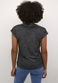 T-shirt noir chiné avec des manches courtes repliées, un col rond et un ourlet légèrement arrondi. Porté avec un jean bleu ajusté.
