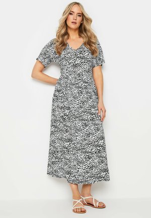 Zwart-witte gestreepte maxi jurk met een V-hals, korte pofmouwen en een cinched taille, gecombineerd met witte sandalen met bandjes.